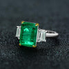 Green Emerald Halo Ring with vivid emerald cut stone, surrounded by a sparkling three stone, perfect for engagements and anniversary
