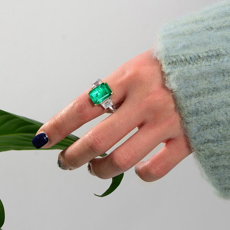 Green Emerald Halo Ring with vivid emerald cut stone, surrounded by a sparkling three stone, perfect for engagements and anniversary
