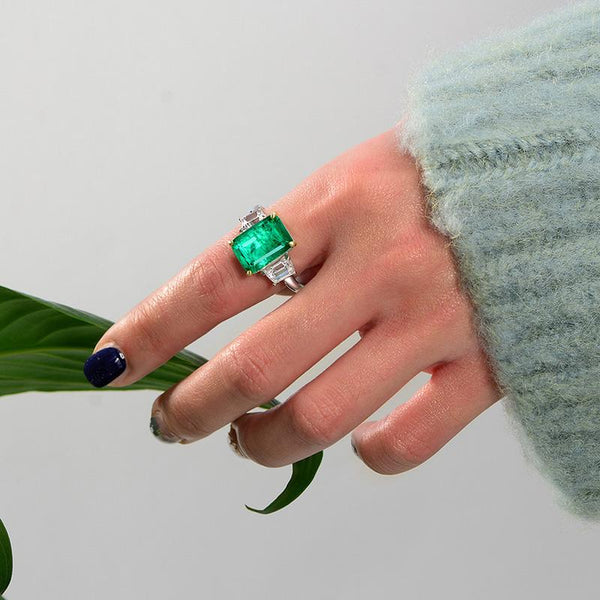 Green Emerald Halo Ring with vivid emerald cut stone, surrounded by a sparkling three stone, perfect for engagements and anniversary